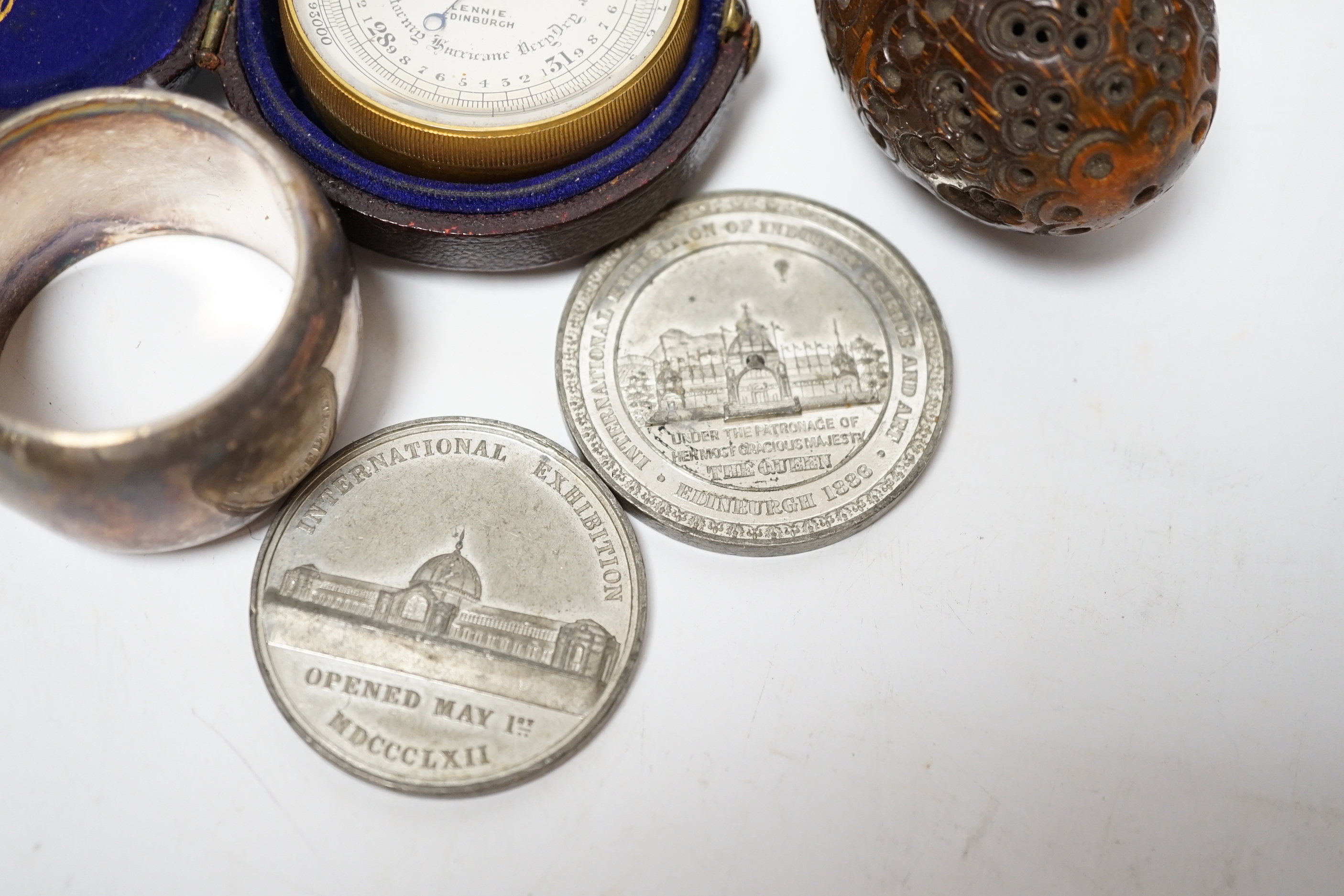 A Lennie brass pocket barometer, a carved coquilla nut, a silver plated napkin ring and two exhibition medallions